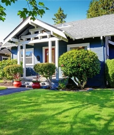 A blue house with green grass and bushes.