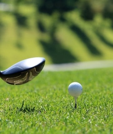 A golf club hitting a ball on the grass.
