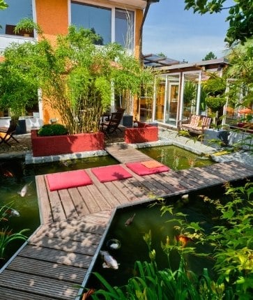 A wooden walkway leads to a pond in a garden.