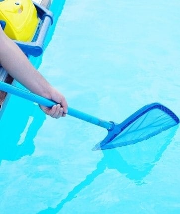 A person holding a broom in a swimming pool.