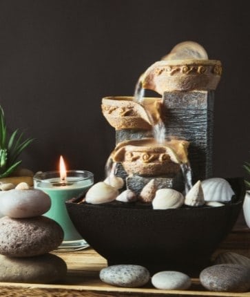 A water fountain with stones and candles on a wooden table.