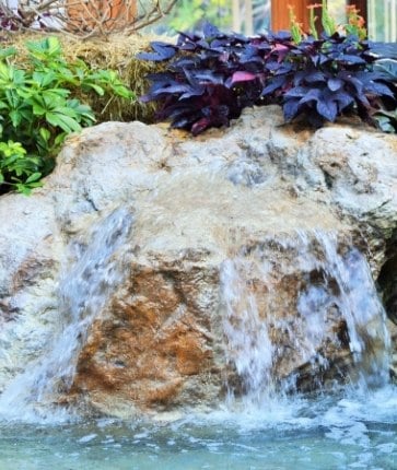 A waterfall in a garden with plants and rocks.