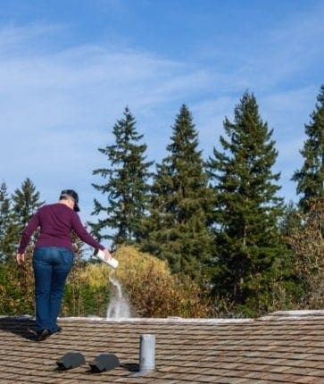 A woman spraying a roof with a hose.