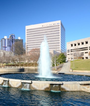 A fountain in the middle of a city with tall buildings in the background.