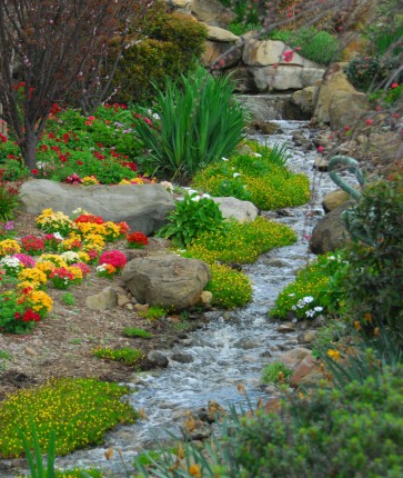 A stream in a garden with flowers and rocks.