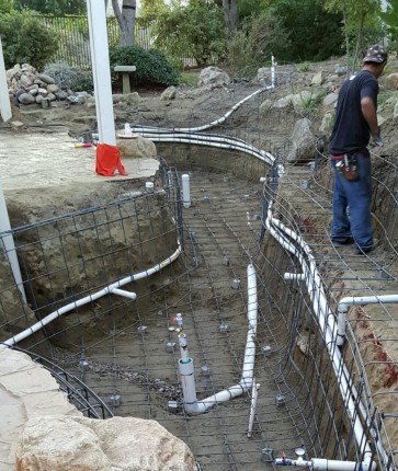 A man is installing a concrete pool in a backyard.