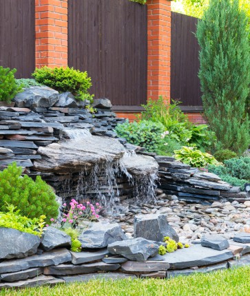 A waterfall in a backyard with rocks and plants.