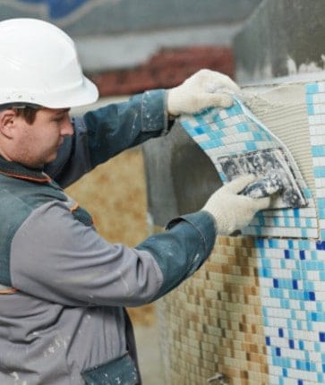 A worker is laying tile on a wall.